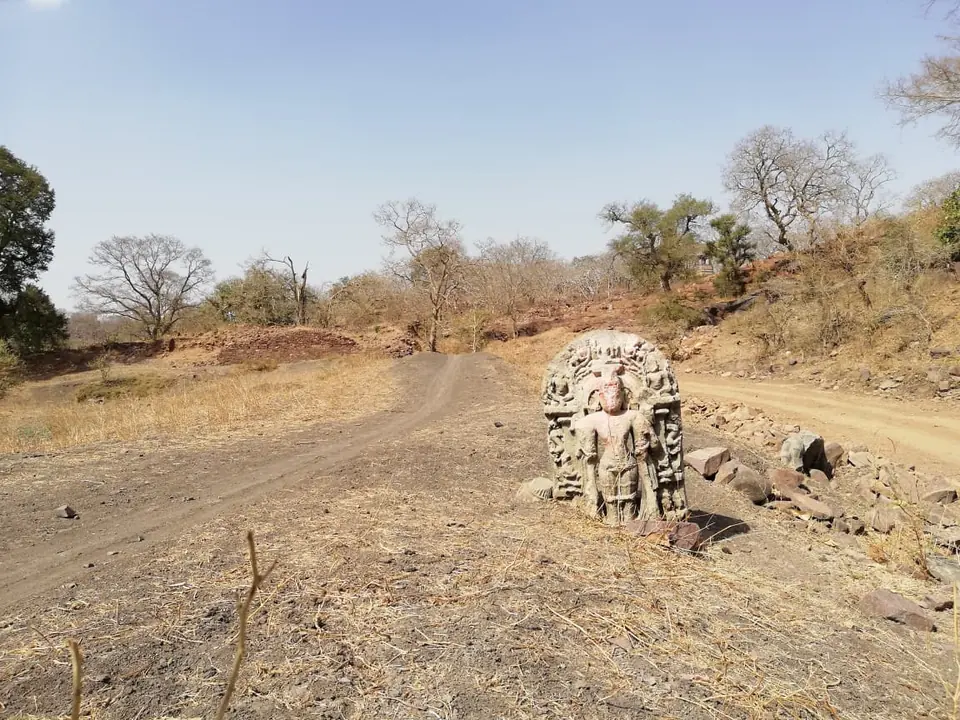 An ancient carved stone figure standing beside a forest path in Mukundara